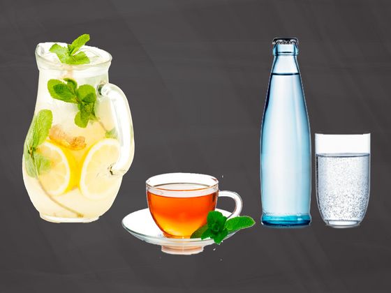Eine Glaskaraffe gefüllt mit Ingwerwasser, eine Tasse Tee und eine Flasche Wasser mit einem Glas stehen nebeneinander auf einer Schiefertafel