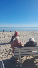Zwei Personen sitzen auf einer Sitzbank am Strand der Ostsee und unterhalten sich mit einer Seniorin bei Gruppenreise nach Zinnowitz an der Ostsee