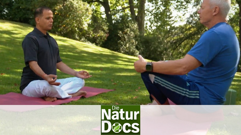 Yogalehrer und Patient sitzen sich im Schneidersitz bei einer Atemübung gegenüber 