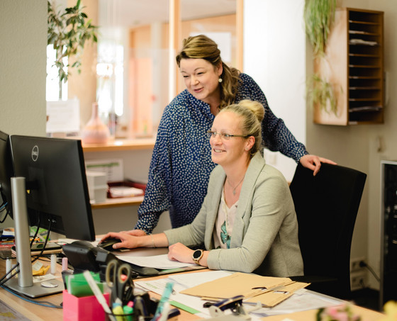 Eine Verwaltungsmitarbeiterin blickt ihrer an einem Schreibtisch sitzenden Kollegin über die Schulter und blickt auf einen Monitor in der Verwaltung der Senioreneinrichtung Immanuel Haus Ecktannen in Waren (Müritz) Eine Verwaltungsmitarbeiterin blickt ihrer an einem Schreibtisch sitzenden Kollegin über die Schulter und blickt auf einen Monitor in der Verwaltung der Senioreneinrichtung Immanuel Haus Ecktannen in Waren (Müritz)