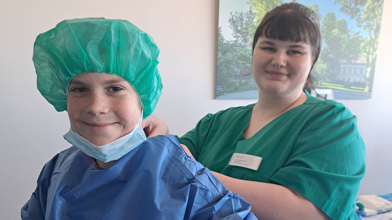 Eine medizinische Fachkraft hilft einem Schüler beim Anziehen des Kasacks, Einblick in den Arbeitsalltag im Krankenhaus, Girls and Boys Day, Immanuel Klinikum Bernau Eine medizinische Fachkraft hilft einem Schüler beim Anziehen des Kasacks, Einblick in den Arbeitsalltag im Krankenhaus, Girls and Boys Day, Immanuel Klinikum Bernau