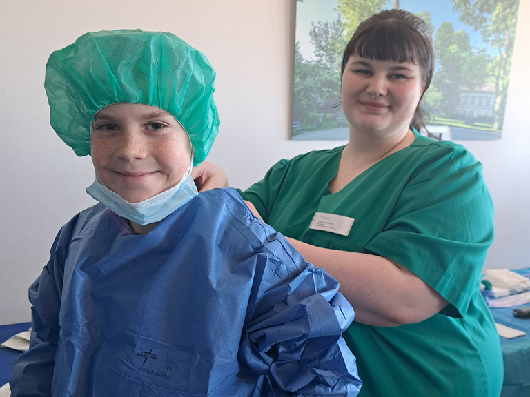 Eine medizinische Fachkraft hilft einem Schüler beim  Anziehen des Kasacks, Einblick in den Arbeitsalltag im Krankenhaus, Girls and Boys Day, Immanuel Klinikum Bernau