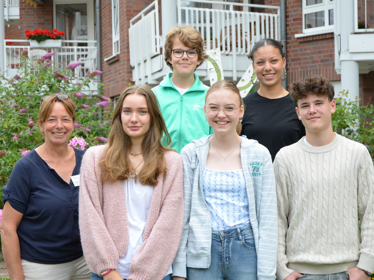Fünf Schülerinnen und Schülern stehen während ihres Sozialpraktikums mit Pflegedienstleitung Karina Arlt  (links) im Sinnesgarten der Residenz am Wiesenkamp in Hamburg-Volksdorf und lächeln beim Gruppenfoto in die Kamera