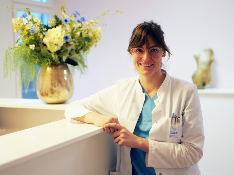 Dr. (univ. Pecs) Zsofia Danckwardt, Leitende Oberärztin Klinik für Gynäkologie und Geburtshilfe sowie Sektionsleiterin Urogynäkologie im Evangelischen Amalie Sieveking Krankenhaus in Hamburg, blickt angelehnt an einen Empfangstresen mit großem Blumenstrauß im Hintergrund in die Kamera Dr. (univ. Pecs) Zsofia Danckwardt, Leitende Oberärztin Klinik für Gynäkologie und Geburtshilfe sowie Sektionsleiterin Urogynäkologie im Evangelischen Amalie Sieveking Krankenhaus in Hamburg, blickt angelehnt an einen Empfangstresen mit großem Blumenstrauß im Hintergrund in die Kamera