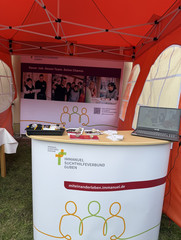 Ein Infostand mit Tisch, Plakat und Informationsmaterial zur Einrichtung und Stellenangeboten beim Fest zum 25-jährigen Jubiläum des Immanuel Suchthilfeverbunds Guben mit besonderen Wohnformen für abhängigkeitskranke Menschen in Thüringen