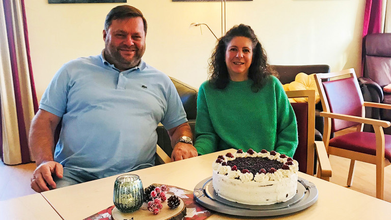 Ehepaar Hahn sitzend am Tisch, auf dem eine Schwarzwälder Kirschtorte steht, ehrenamtliches Engagement, freiwillige Mitarbeit, Albertinen Hospiz Norderstedt Ehepaar Hahn sitzend am Tisch, auf dem eine Schwarzwälder Kirschtorte steht, ehrenamtliches Engagement, freiwillige Mitarbeit, Albertinen Hospiz Norderstedt