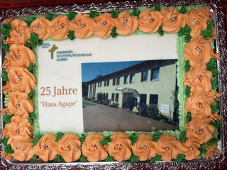 Ein großer quadratischer Kuchen mit essbaren Rosen und Foto und Schrift aus Zuckerguss zum 25-jährigen Jubiläum des Immanuel Suchthilfeverbunds Guben mit besonderen Wohnformen für abhängigkeitskranke Menschen in Thüringen