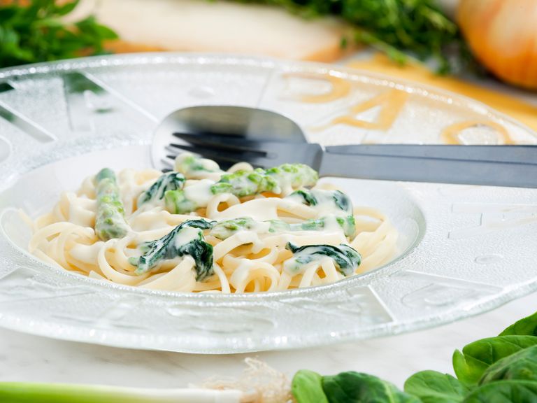 Linguini mit grünem Spargel, Ruccola & gerösteten Pinienkernen an Safransauce angerichtet auf einem weißen Teller