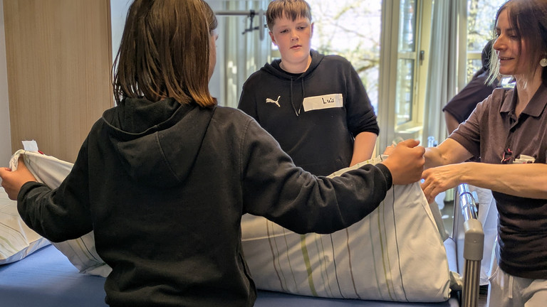 Junge hebt fertig bezogene Bettdecke an - Boys Day bei Immanuel Dienstleistungen Junge hebt fertig bezogene Bettdecke an - Boys Day bei Immanuel Dienstleistungen