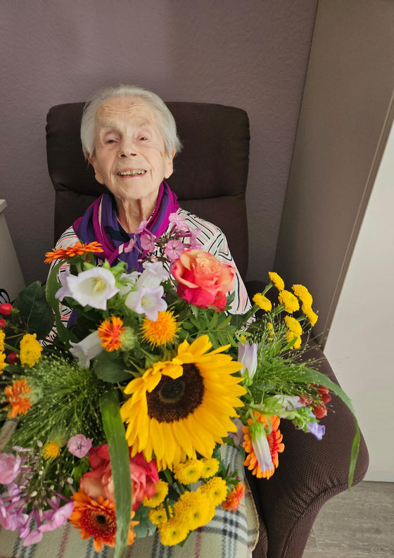Bewohnerin mit Blumenstrauß sitzt im Sessel Bewohnerin mit Blumenstrauß sitzt im Sessel