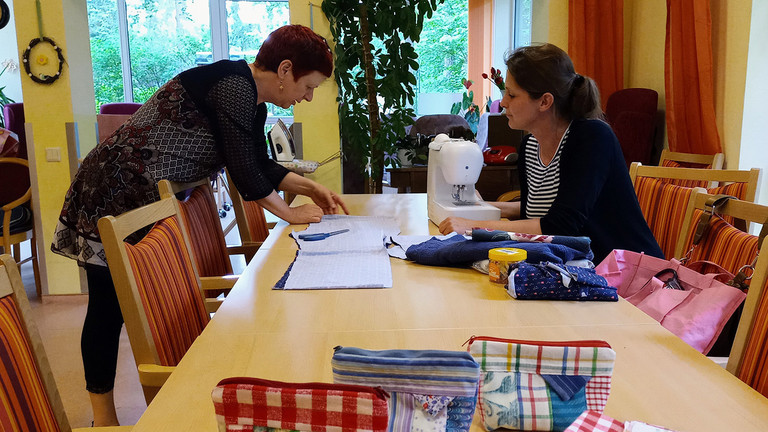 Kursleiterin zeigt Teilnehmerin, wie die Stoffteile vor dem Nähen korrekt zusammengelegt werden - Nähkurs- Räume Tagespflege Immanuel Haus Ecktannen Kursleiterin zeigt Teilnehmerin, wie die Stoffteile vor dem Nähen korrekt zusammengelegt werden - Nähkurs- Räume Tagespflege Immanuel Haus Ecktannen