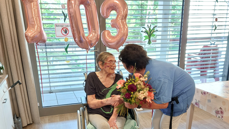 Bewohnerin im Rollstuhl bekommt Blumen von Pflegerin überreicht Bewohnerin im Rollstuhl bekommt Blumen von Pflegerin überreicht