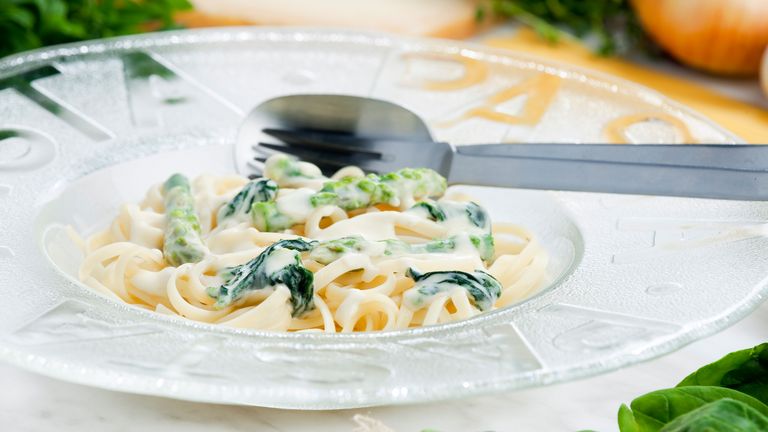 Linguini mit grünem Spargel, Ruccola & gerösteten Pinienkernen an Safransauce angerichtet auf einem weißen Teller