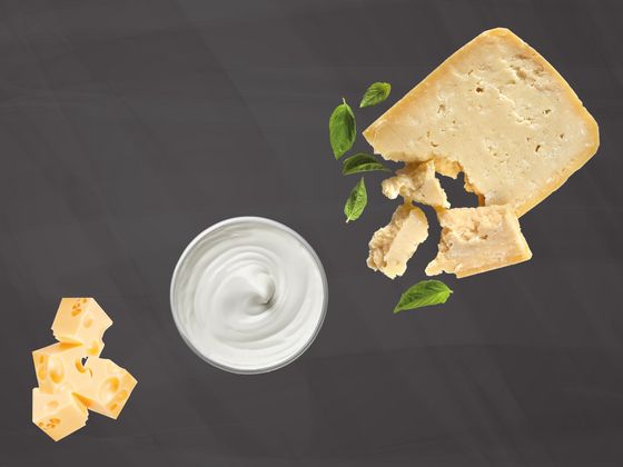 Zwei verschiedene Sorten Käse und ein Töpfchen Joghurt auf einer Schiefertafel