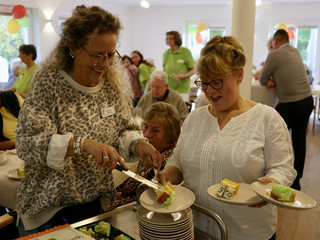 Eine Mitarbeiterin reicht einer Frau Kuchen auf mehrere Teller bei der Wiedereröffnung der Tagespflegestätte für ältere Menschen im Immanuel Seniorenzentrum Kläre Weist in Petershagen Eine Mitarbeiterin reicht einer Frau Kuchen auf mehrere Teller bei der Wiedereröffnung der Tagespflegestätte für ältere Menschen im Immanuel Seniorenzentrum Kläre Weist in Petershagen