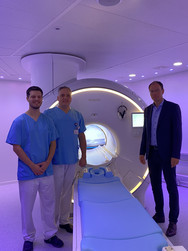 Richard Grundherr, Prof. Christoph Weber und Andreas Schneider stehen in einem dunkellila illuminierten Raum vor dem neuen MRT-System im Immanuel Albertinen Zentrum für Radiologie am Standort Ev. Amalie Sieveking Krankenhaus in Hamburg und blicken in die Kamera