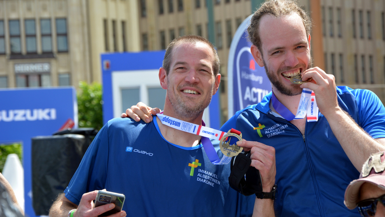 Zwei Teilnehmer mit Medaille beim Zieleinlauf World Triathlon Sprint & Relay Championships in Hamburg, Firmencup, Triathlon, Sportevent Mitarbeitende, Immanuel Albertinen Diakonie, Hamburg, Berlin, Brandenburg Zwei Teilnehmer mit Medaille beim Zieleinlauf World Triathlon Sprint & Relay Championships in Hamburg