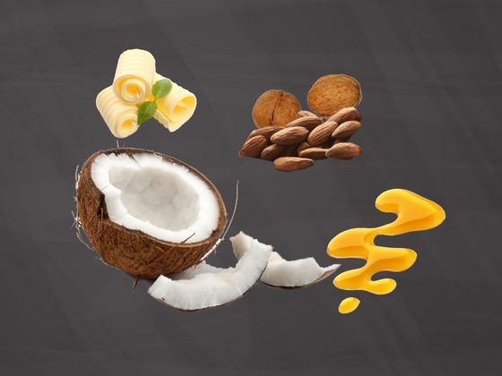 Eine halbe Kokosnuss, Butter, Mandeln und Walnüsse, sowie Öl auf einer Schiefertafel