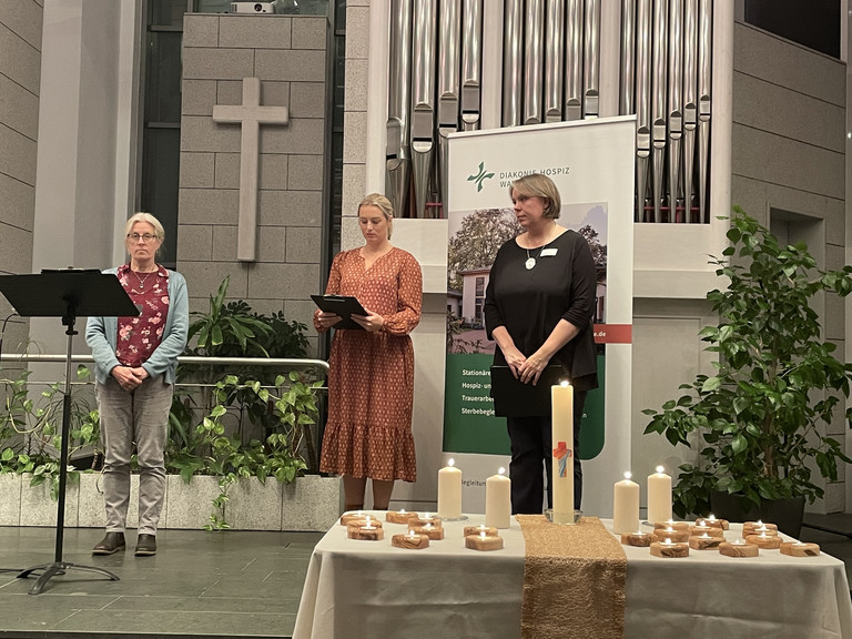 Pastorin Witzemann und zwei Mitarbeiterinnen auf der Bühne in der Kirche, Gottesdienst in Gedenken an die Verstorbenen, Ambulanter Hospizdienst, stationäres Hospiz, Diakonie Hospiz Wannsee, Berlin