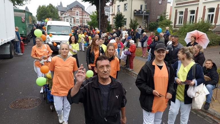 Mitarbeitende auch in Funktionskleidung laufen vor dem Transporter beim Festumzug zum Jubiläums-Müritzfest mit Pflegekräften, Bewohnerinnen und Bewohnern aus dem Immanuel Haus Ecktannen Mitarbeitende auch in Funktionskleidung laufen vor dem Transporter beim Festumzug zum Jubiläums-Müritzfest mit Pflegekräften, Bewohnerinnen und Bewohnern aus dem Immanuel Haus Ecktannen