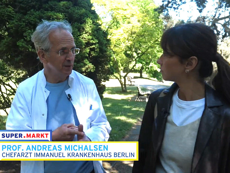Screenshot Pro. Michalsen im Gespräch mit Frau im Park und einer Bauchbinde der Sendung
