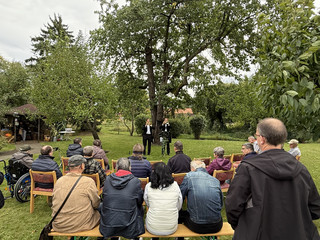 Menschen sitzen auf Stuhlreihen im Freien und verfolgen eine Rede beim Fest zum 25-jährigen Jubiläum des Immanuel Suchthilfeverbunds Guben mit besonderen Wohnformen für abhängigkeitskranke Menschen in Thüringen