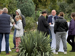 Mitarbeitende und Gäste stehen im Freien an zwei Tischen und unterhalten sich beim 25-jährigen Jubiläum des Immanuel Suchthilfeverbunds Guben mit besonderen Wohnformen für abhängigkeitskranke Menschen in Thüringen