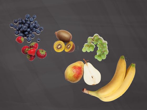 Komposition aus Weintrauben, Him-, Erd- und Heidelbeeren, Bananen, Äpfeln, Kiwis und Birnen auf einer Schiefertafel