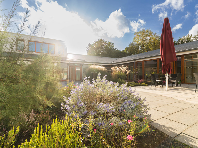 Blick auf die Vorderansicht mit Terrasse des Diakonie Hospiz Norderstedt bei blauem Himmel und Sonnenschein mit Pflanzen und Sträuchern im Vordergrund Blick auf die Vorderansicht mit Terrasse des Diakonie Hospiz Norderstedt bei blauem Himmel und Sonnenschein mit Pflanzen und Sträuchern im Vordergrund